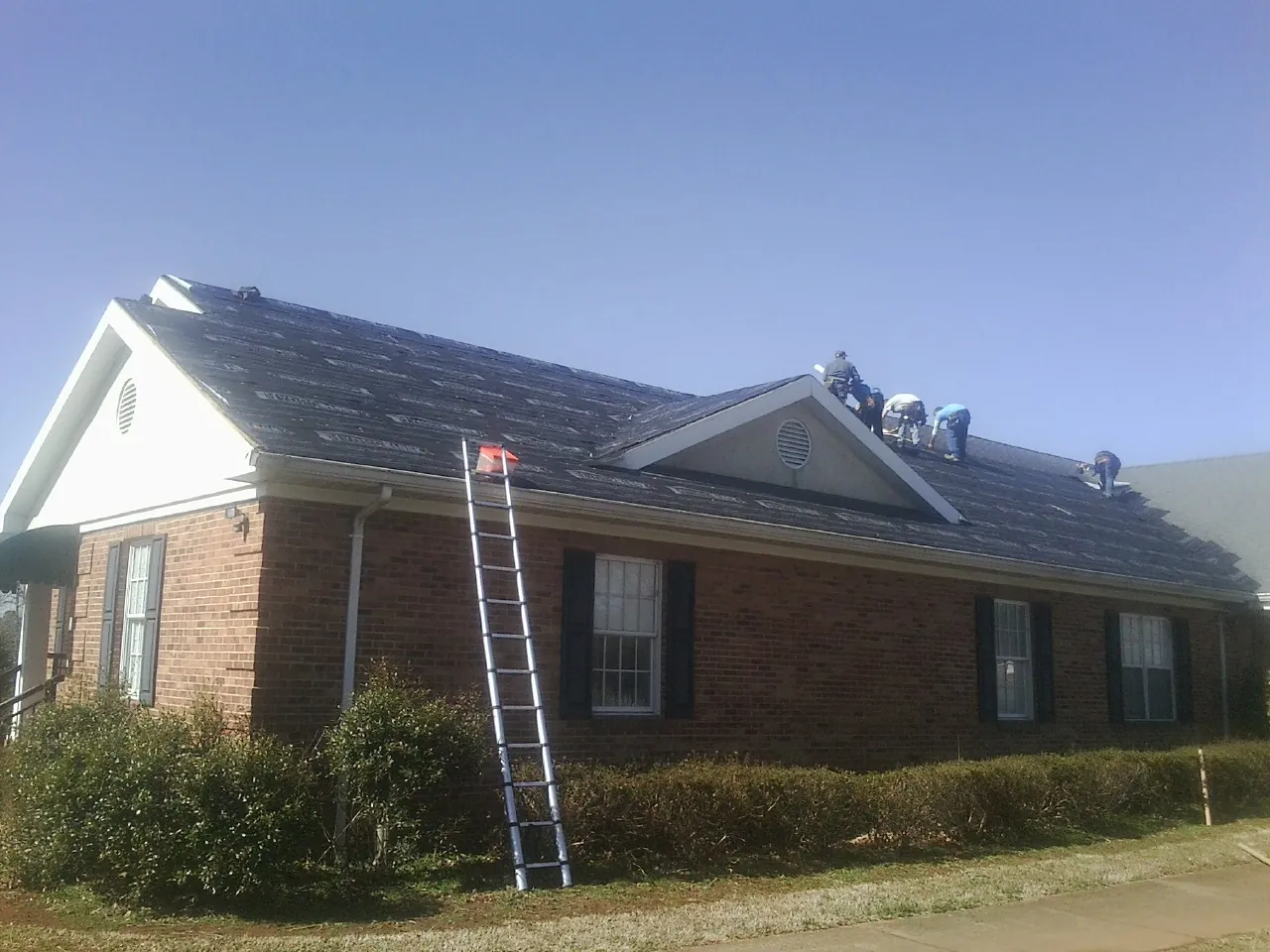 Crew tearing shingles off a brick ranch roof with a ladder set — Metal Roof Repair work by our crew in Green Springs