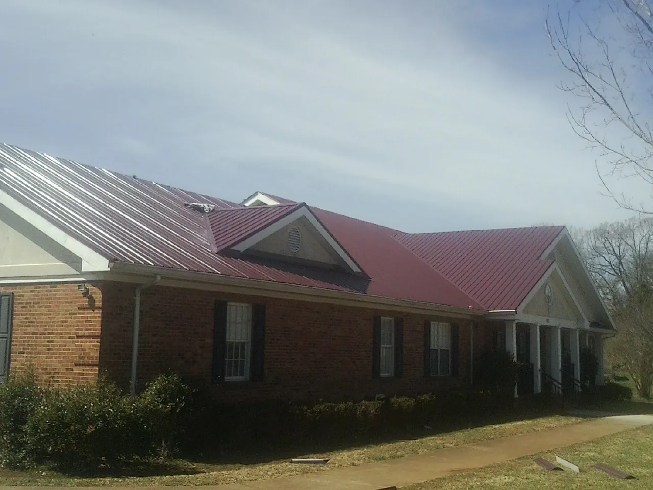 Red metal roof with gabled entries on a long brick building, from a Hail Damage Roof Repair job in Green Springs
