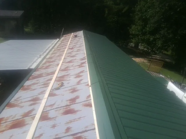 Old rusted panels beside newly installed green metal roofing — Wind Damage Roof Repair by Roofing Brothers in Green Springs