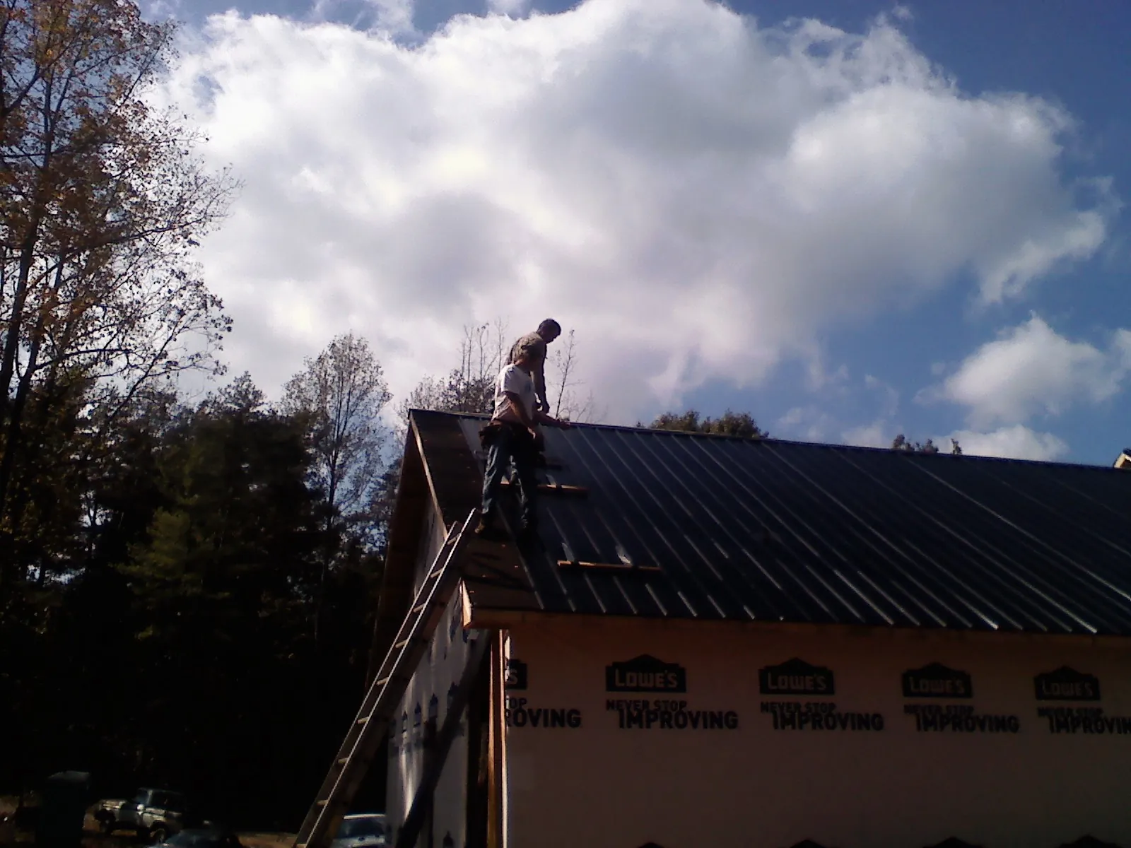 Roofer fastening dark metal panels high against a cloudy sky, from a Roof Inspection job in Green Springs