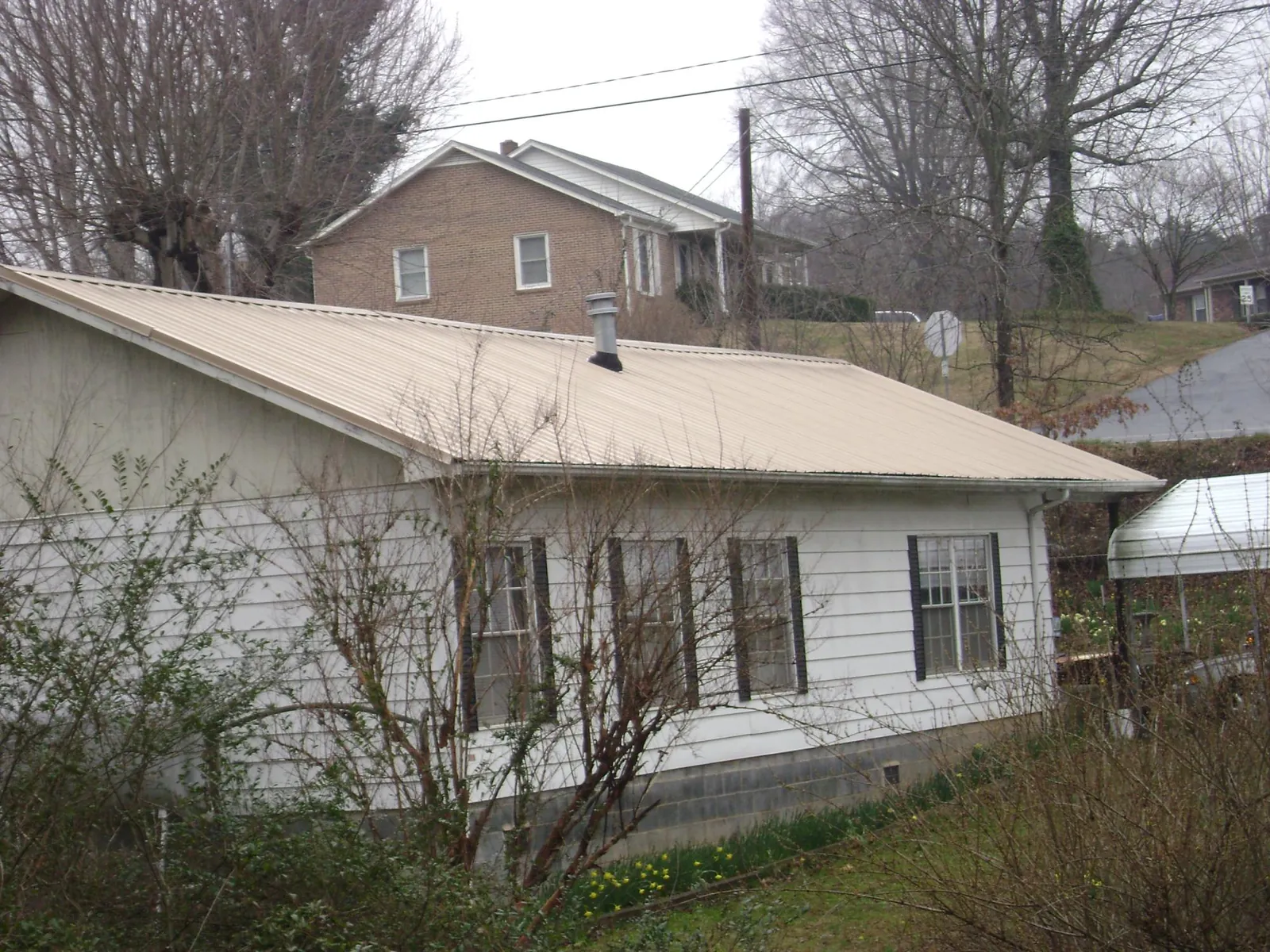 Tan metal roof on a white sided house set into a hillside — Commercial Roofing by Roofing Brothers in Green Springs